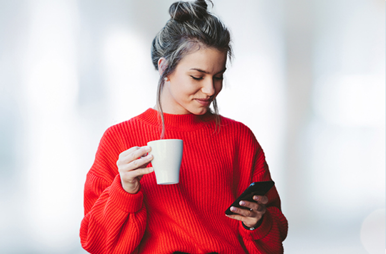 Photo d’une femme qui boit un café en consultant son cellulaire  
